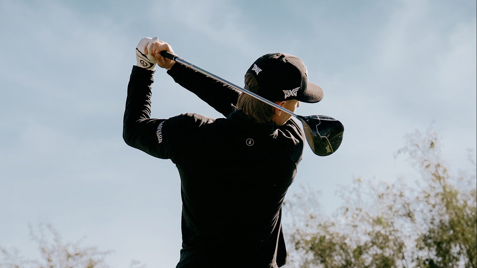 Person in black outfit and cap holding a golf club against a clear sky