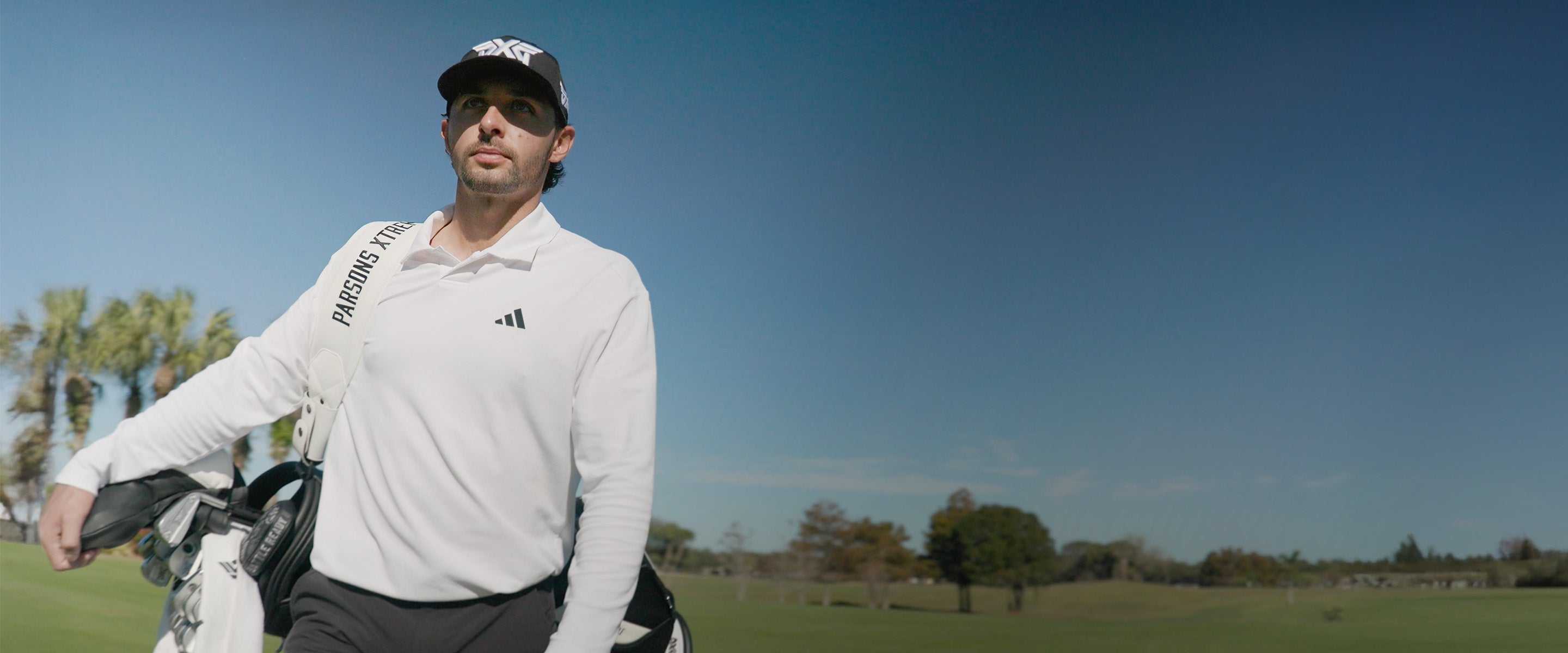 Marco Penge wearing a black PXG hat on a golf course.