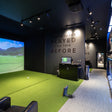 Golf simulator room with green turf, screen displaying a golf course