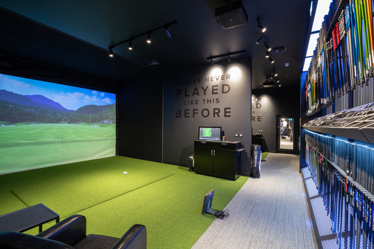Golf simulator room with green turf, screen displaying a golf course