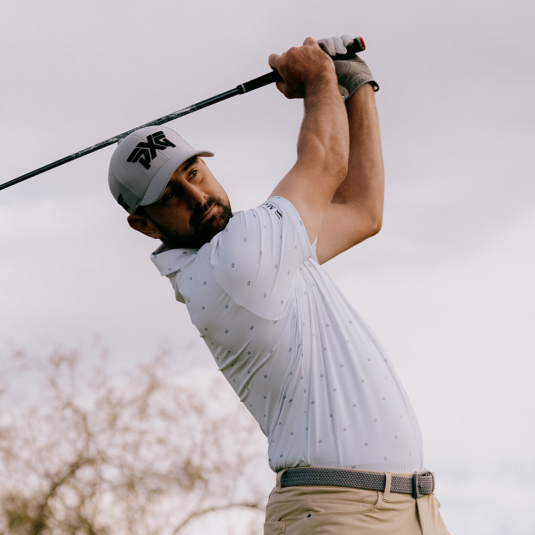 Pro Cristobal Del Solar wearing a PXG Hat and swinging a golf club on a golf course.