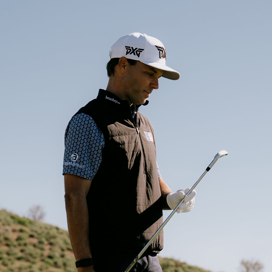 PGA Tour Pro Eric Cole wearing a PXG Golf Hat on a golf course and holding a golf club.