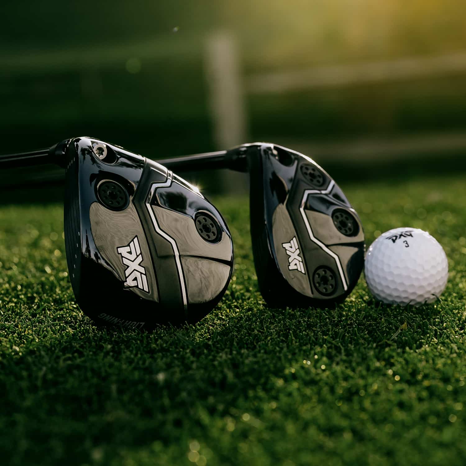 Two black and silver golf clubs with white PXG logos resting on green grass next to a white golf ball.