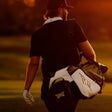 A golfer seen from behind on a golf course at sunset, carrying a white and black golf bag with a visible Callaway logo.
